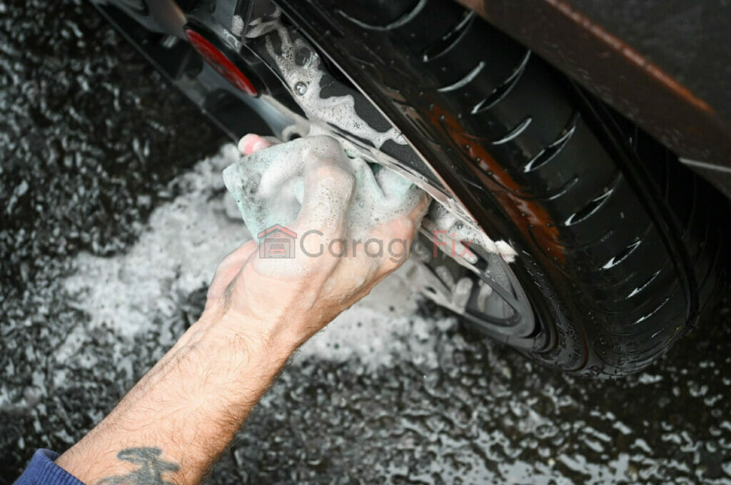 A man washing a car tire with a sponge.