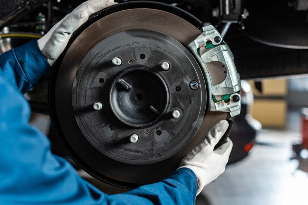 Mechanic with white gloves installs a brake disc and caliper onto a vehicle in a workshop.